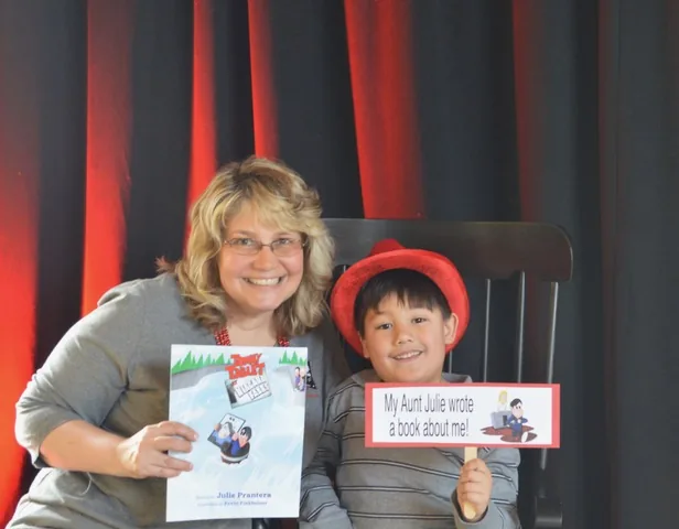 Julie Prantera holding Tommy Tablet at Niagara Falls beside her nephew Nathan, who wears a red hat and holds a sign reading My Aunt Julie wrote a book about me.