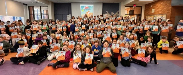 A large school assembly of students holding copies of Tommy Tablet Takes Australia.