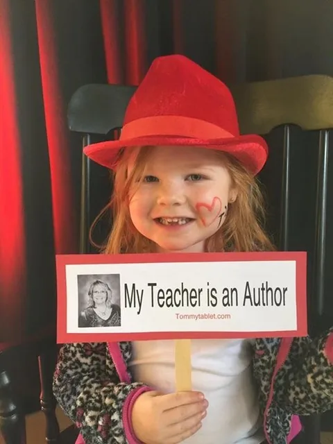 A smiling young girl in a red hat holding a sign that reads My Teacher is an Author, with Julie Prantera's photo and tommytablet.com.